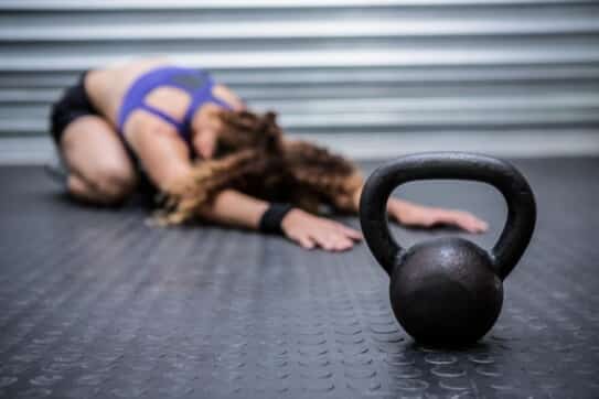 Femme faisant des étirement à la fin de sa séance de sport, à côté d'une kettle bell.